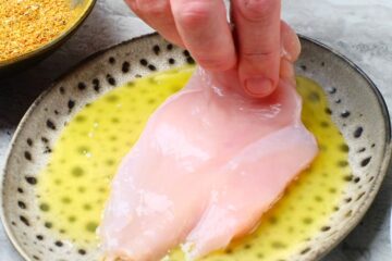 Raw chicken breast in a plate of melted butter.