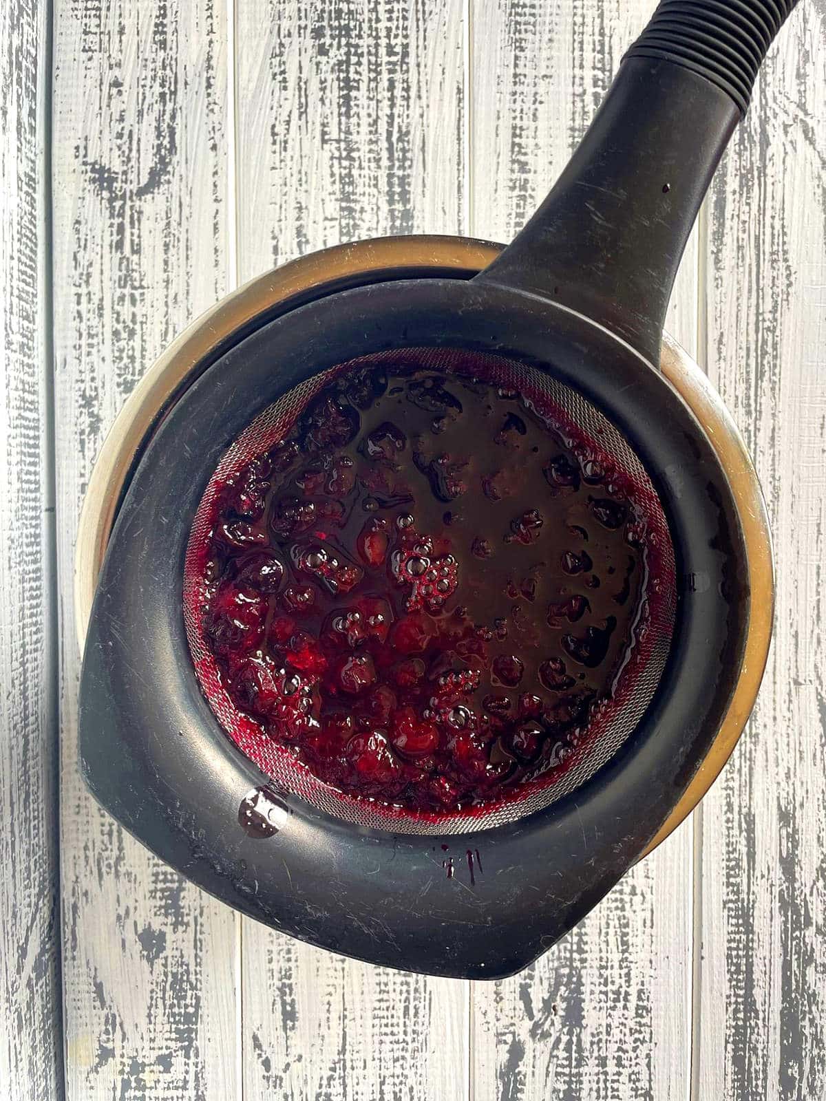 Blueberry sugar syrup in mesh strainer.