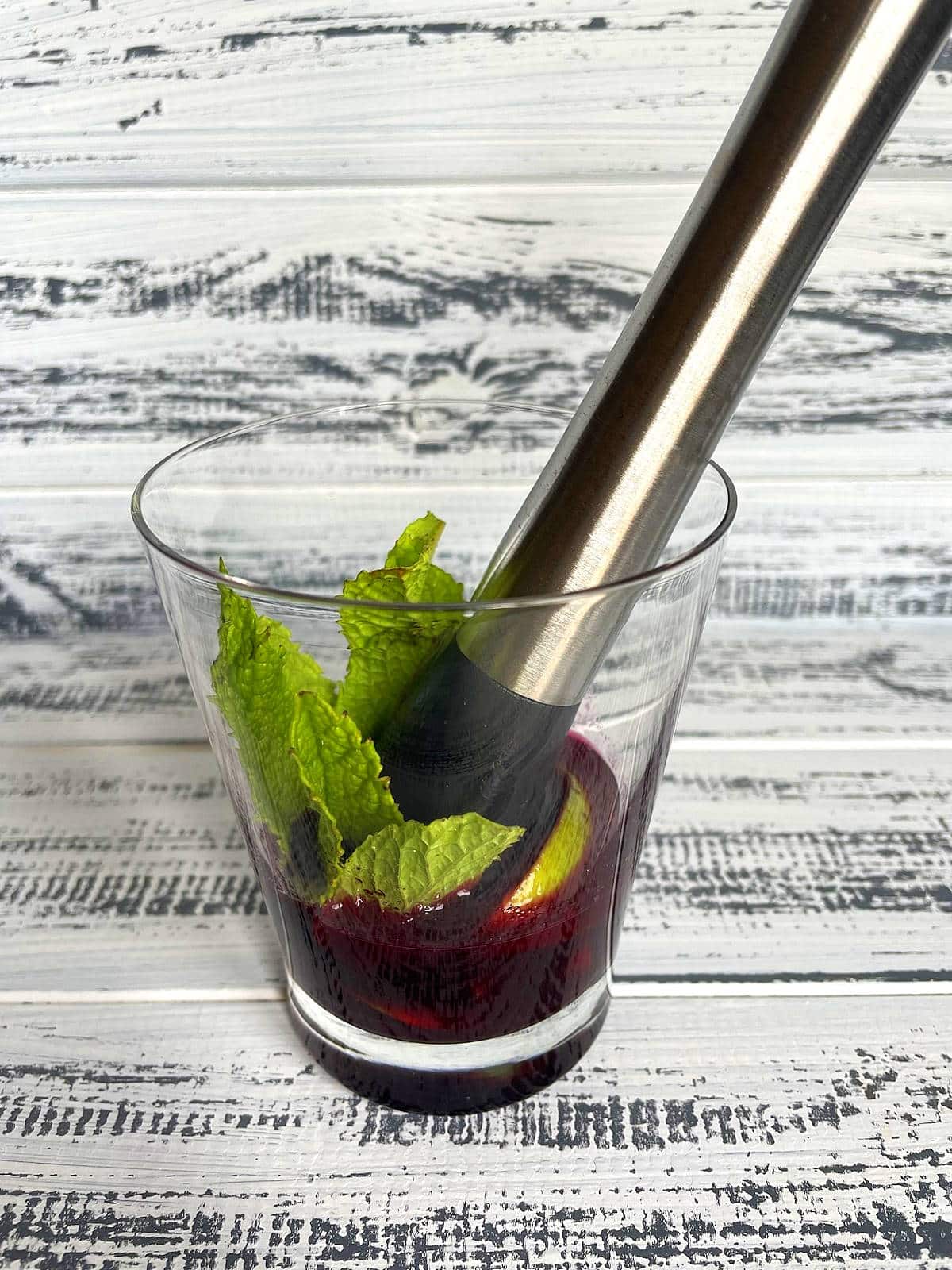 Mint, limes and syrup in glass with muddler.