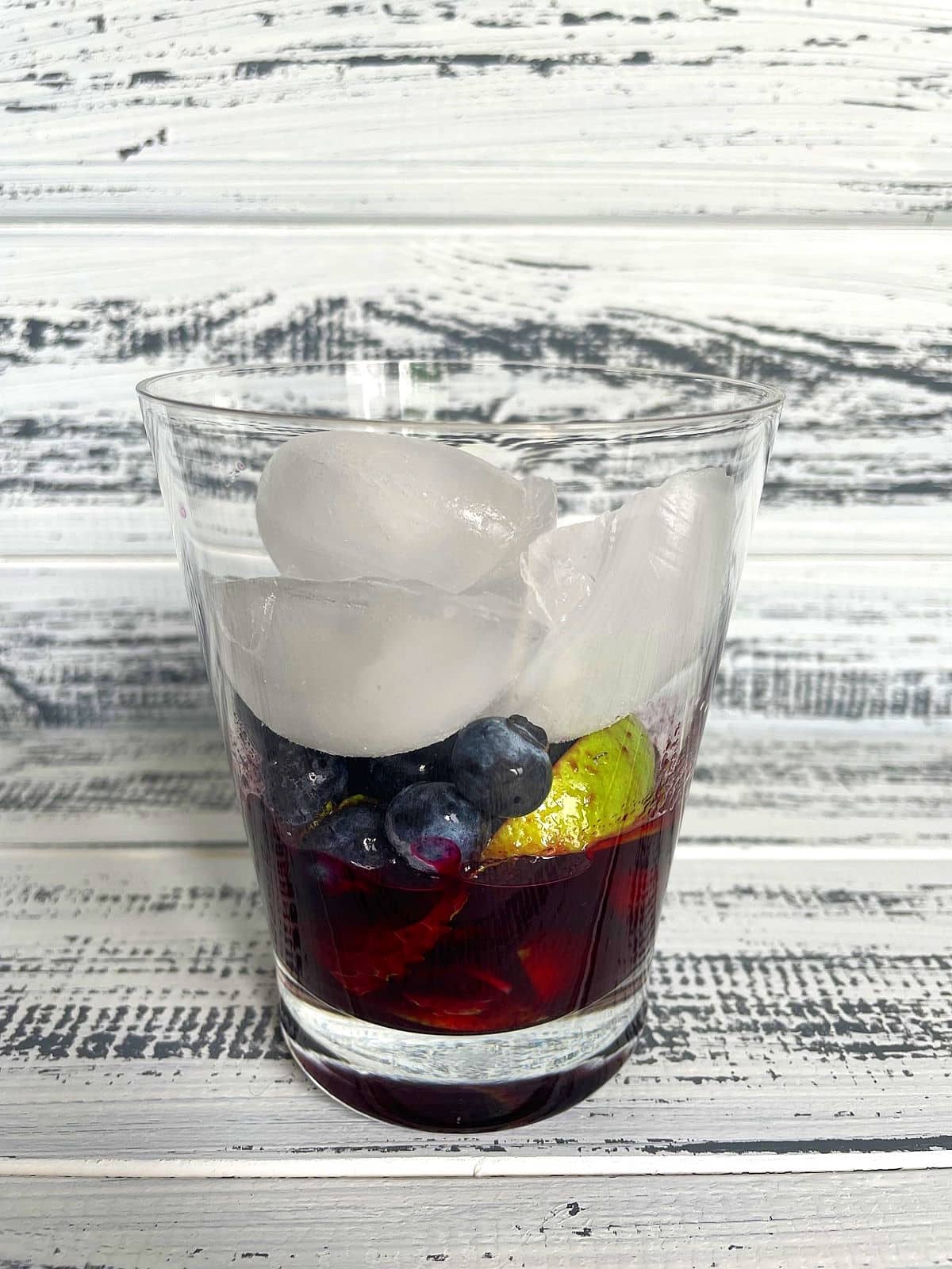 Ice cubes, blueberries, limes, mint and syrup in cocktail glass.