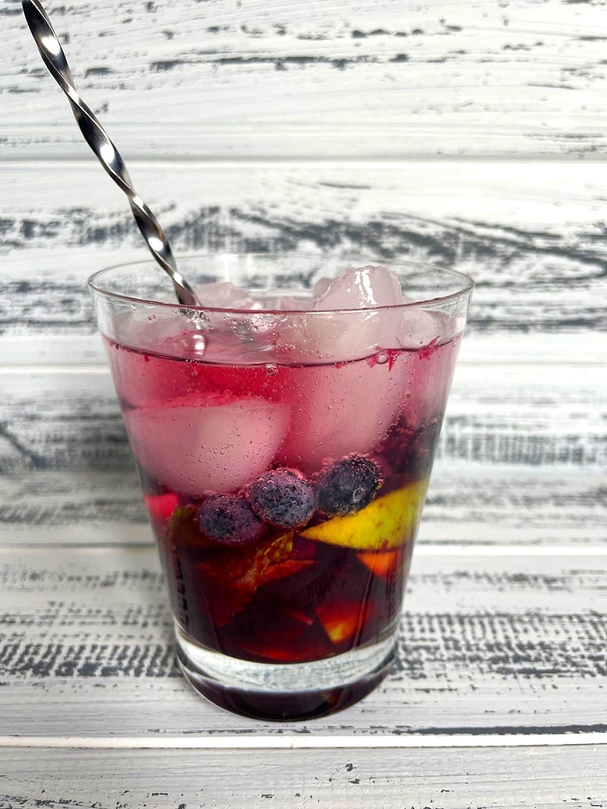 Blueberry mojito mocktail ingredients in cocktail glass with bar stir stick.