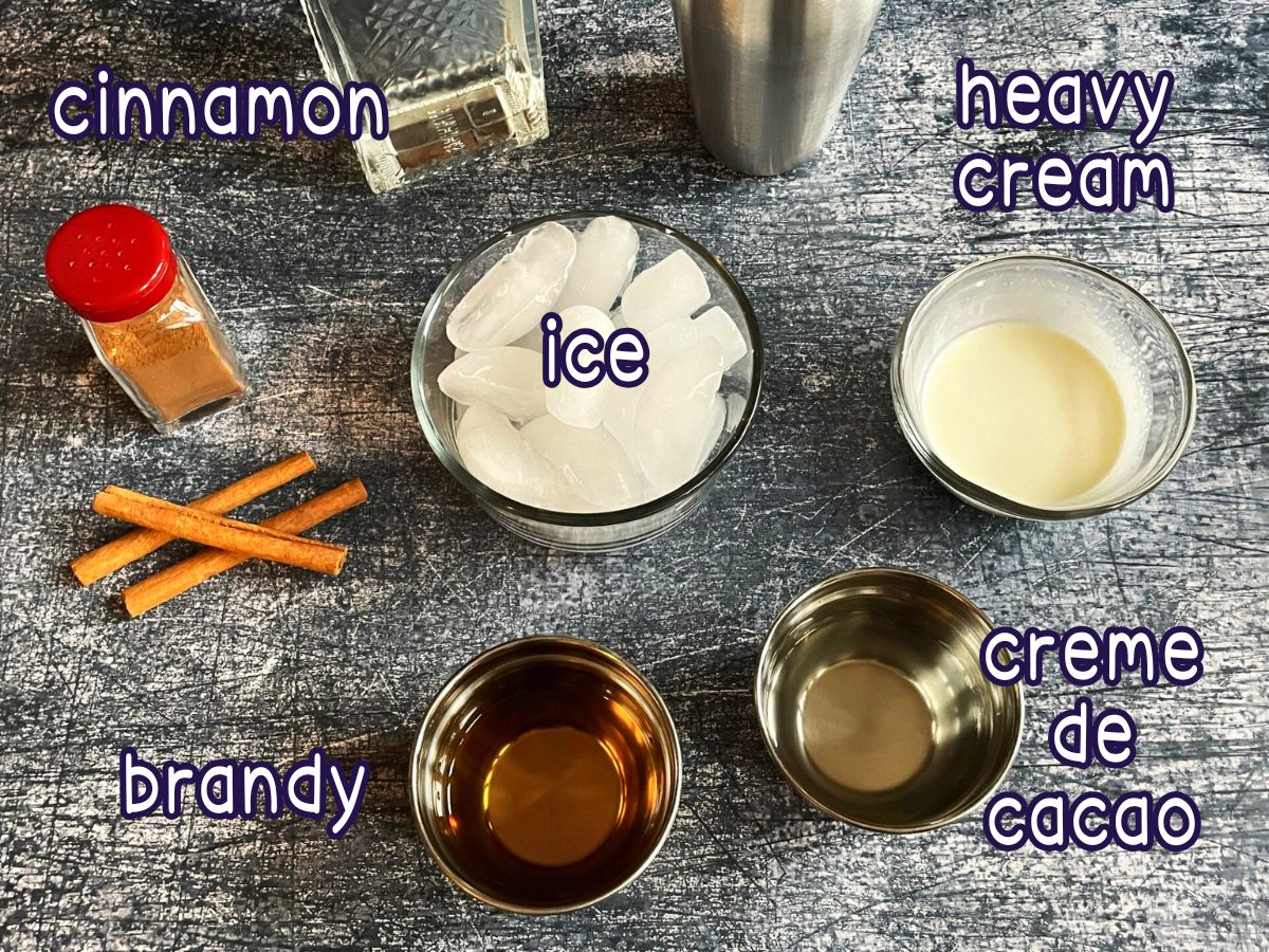 Brandy Alexander cocktail ingredients prepped and labeled on blue background.