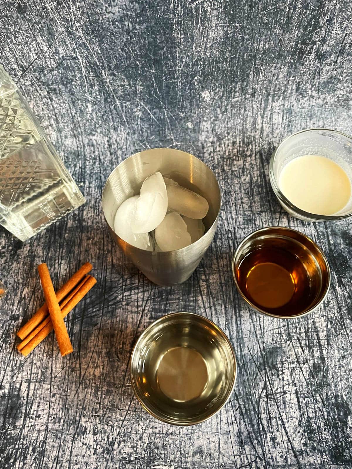 Cocktail shaker filled with ice, surrounded by Brandy Alexander ingredients.