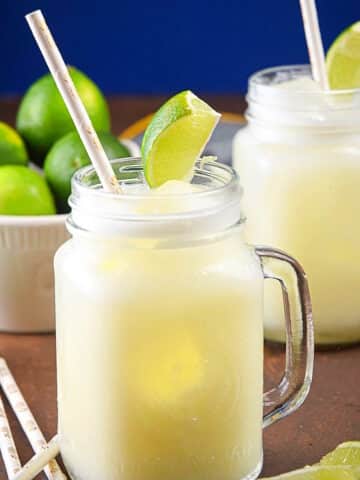 Brazilian lemonade in glasses with straws and lime wedges.