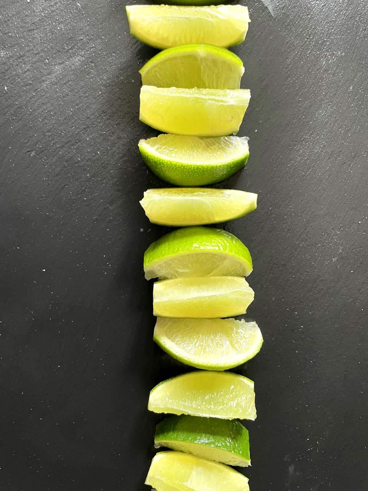 Lime wedges with pith removed in a row on black board.