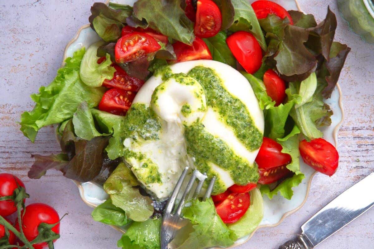 Burrata cheese cut open over greens and tomatoes on plate.