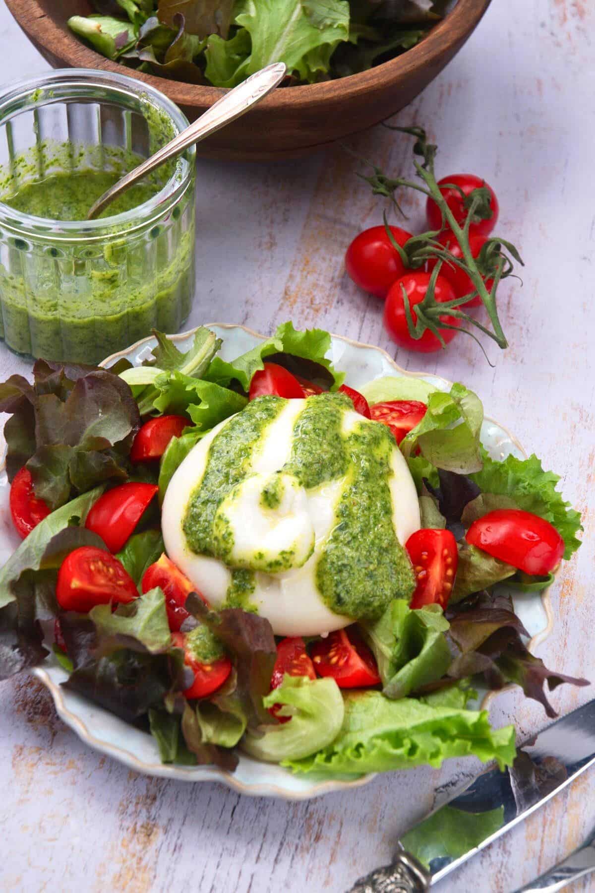 Burrata salad with pesto dressing on plate and pesto dressing on the side.