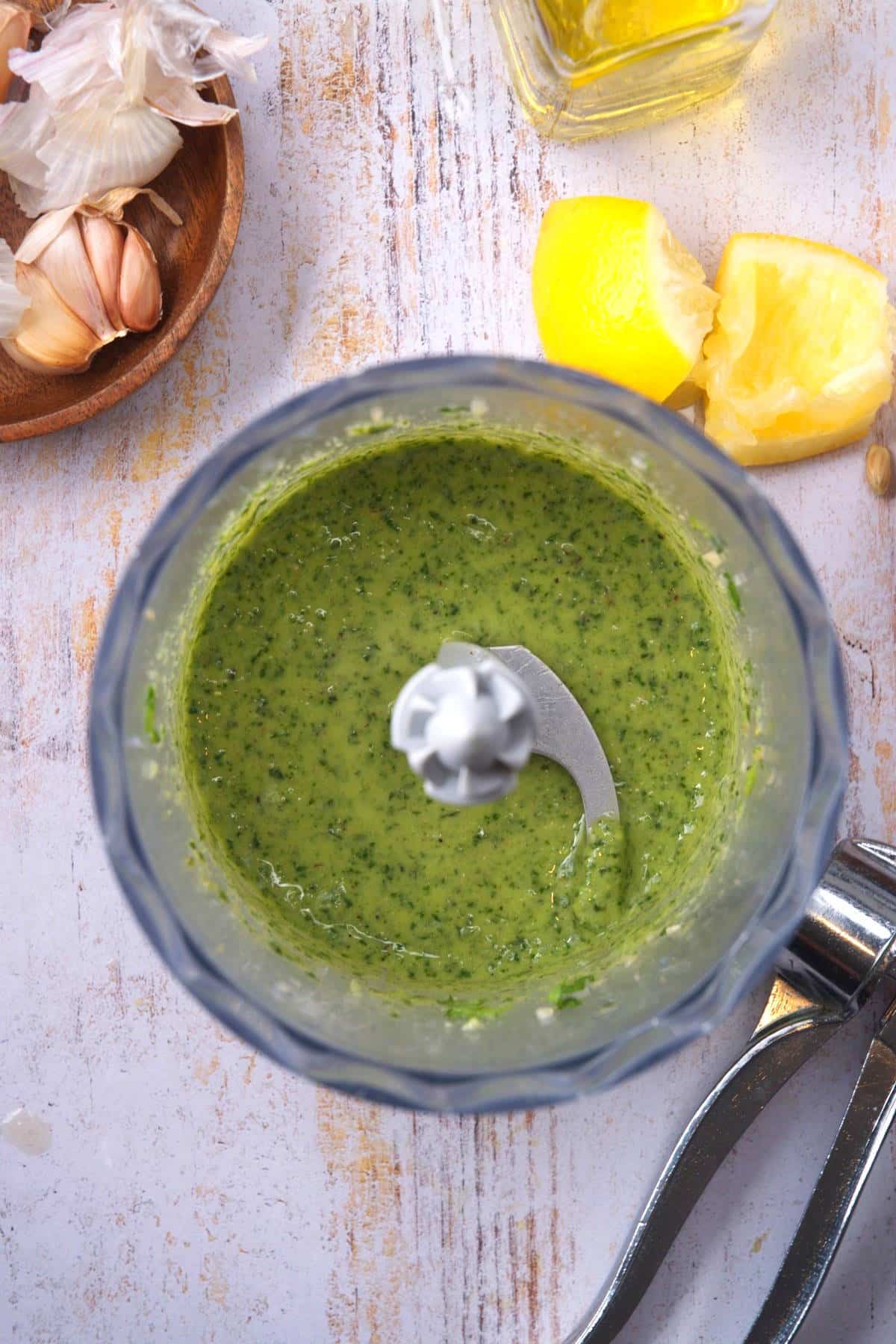 Basil pesto in food processor with squeezed lemons on the side.