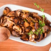 Sauteed mushrooms and onions in white dish with fresh thyme sprigs.