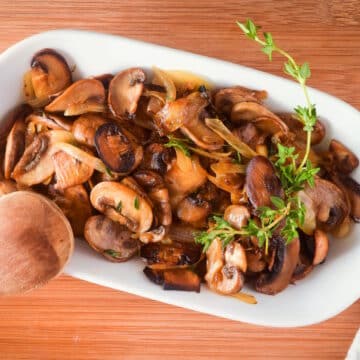 Sauteed mushrooms and onions in white dish with fresh thyme sprigs.