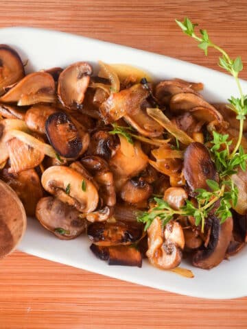 Sauteed mushrooms and onions in white dish with fresh thyme sprigs.