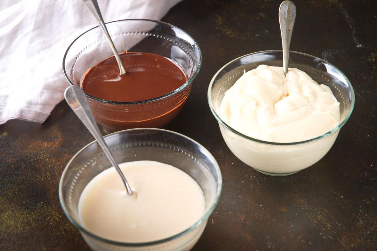 Cake pop frosting, icing and chocolate coating in bowls with spoons.