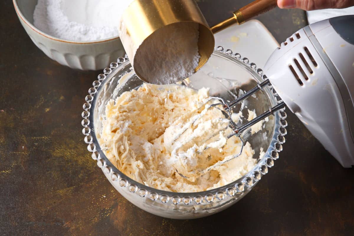 Cream cheese frosting with powdered sugar in bowl with electric mixer.