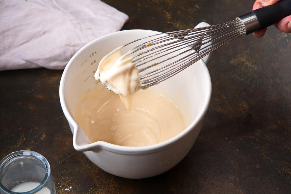 Cake pop icing on whisk over bowl.