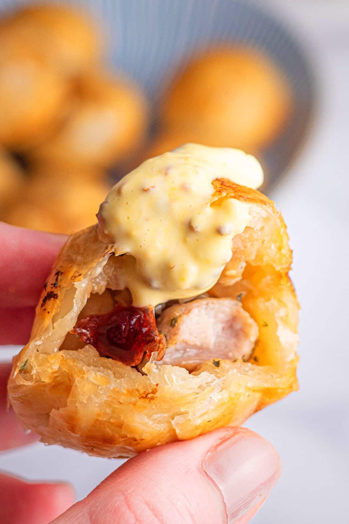 Puff pastry chicken ball cut open and dipped in mustard sauce.