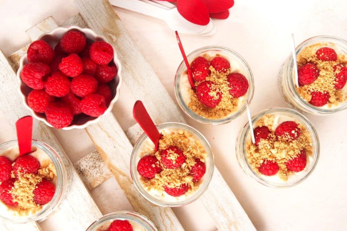 Canada Day raspberry cheesecake in jars with red and white spoons and fresh raspberries on the side.
