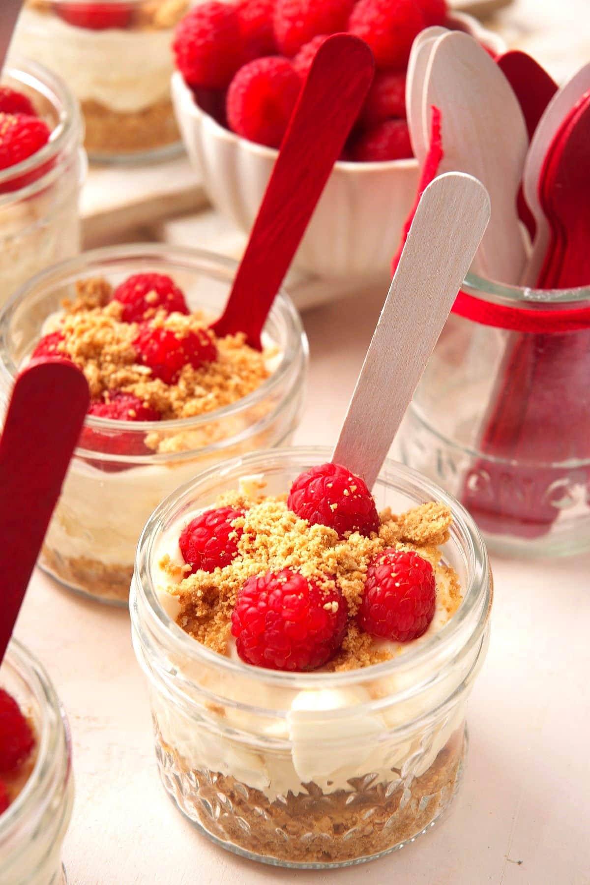 Canada Day raspberry cheesecake in jars with red and white spoons and fresh raspberries.