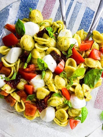 Caprese pasta salad with pesto on clear plate.