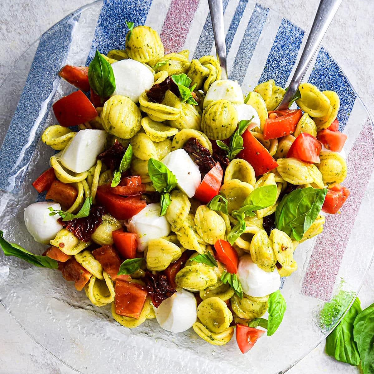 Caprese pasta salad with pesto on clear plate.