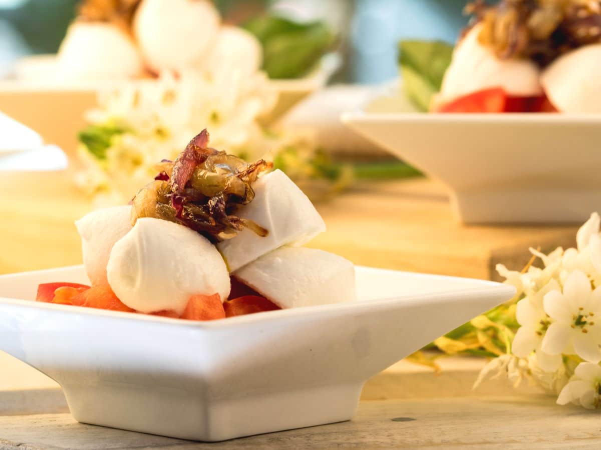 Caprese salad with cherry tomatoes, balsamic and caramelized onions in white dish.