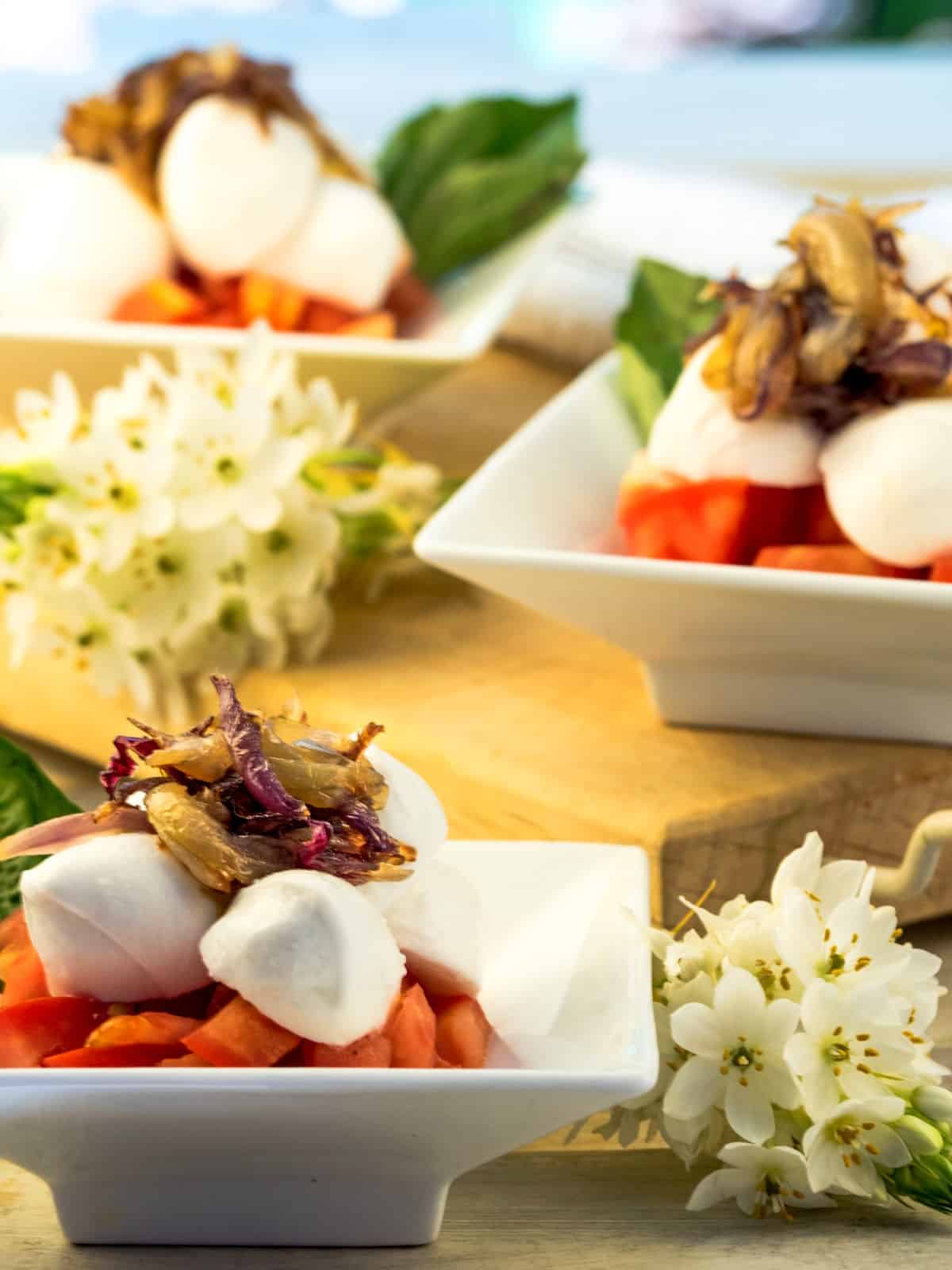 Caprese salad stacked in small, white dishes.