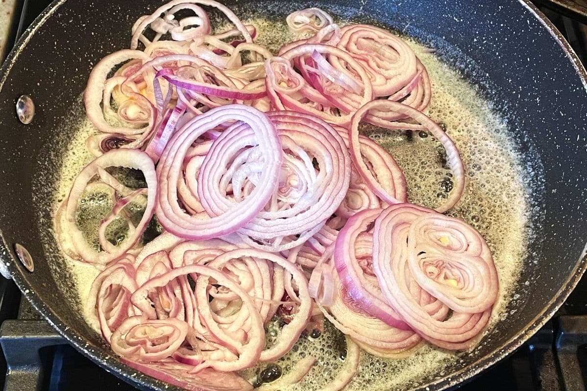 Red onions slices in pan with melted butter.