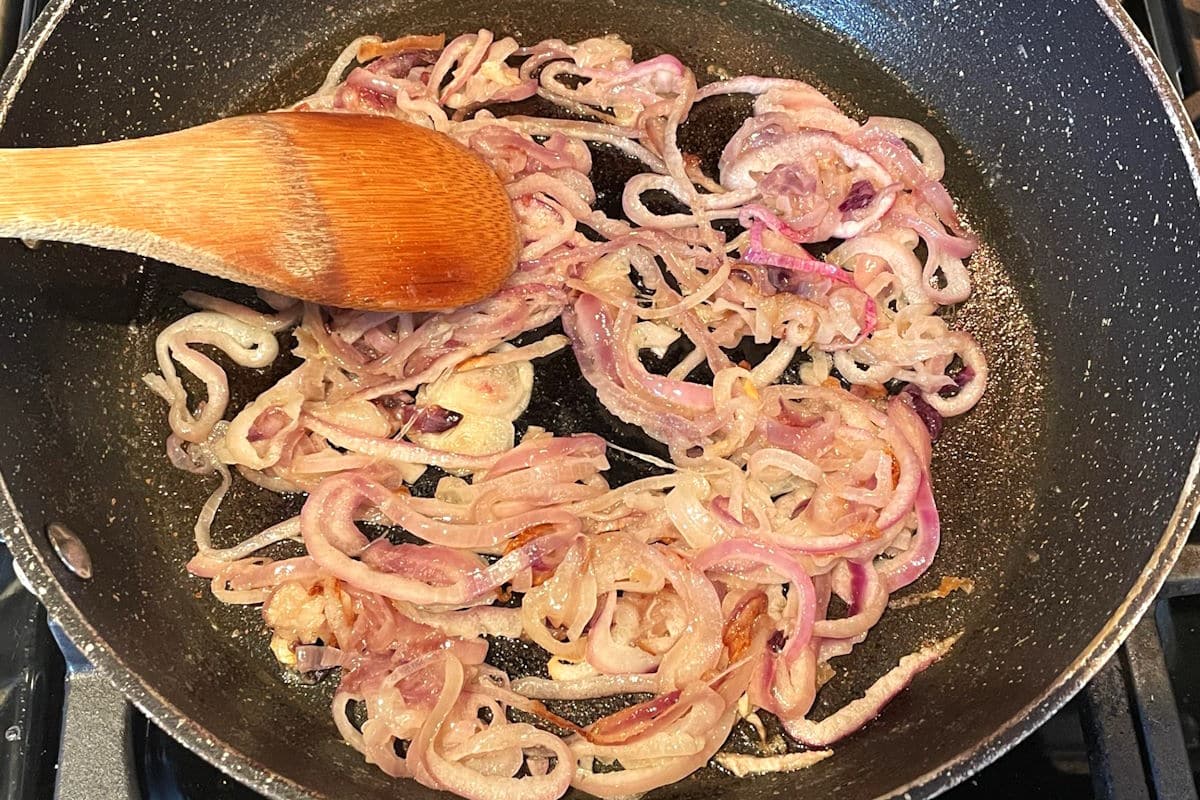 Red onions caramelizing in pan.