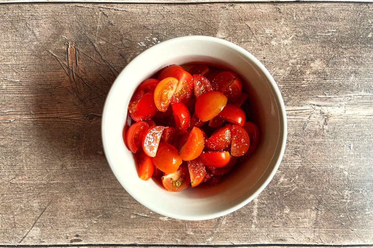 Cherry tomatoes combined with salt and olive oil in small dish.