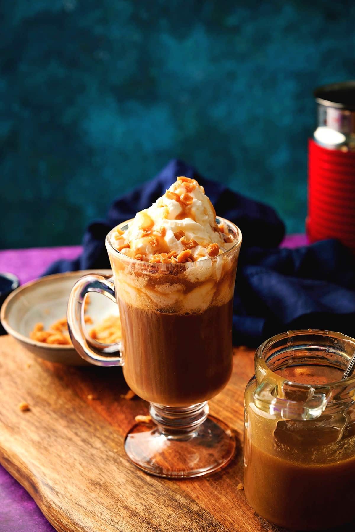 Caramel brûlée latte in a mug and a jar of caramel sauce on the side on wooden board.
