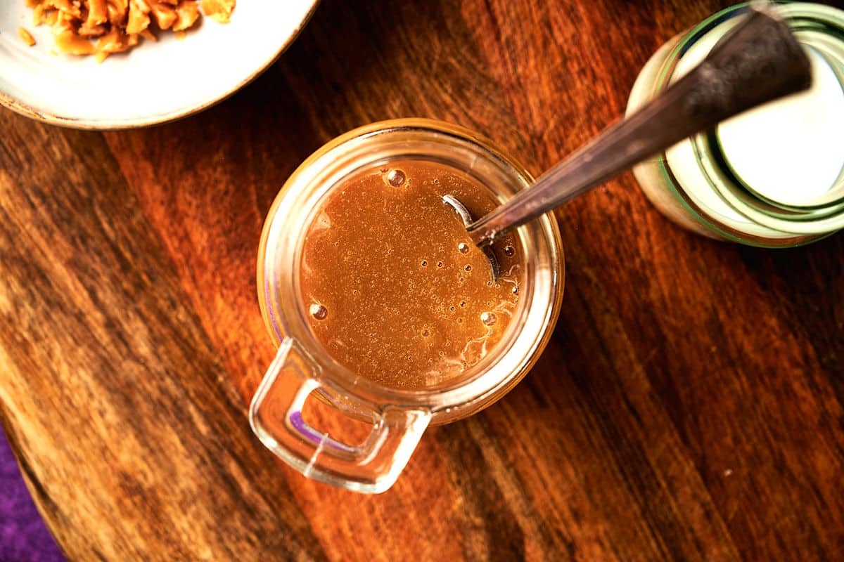 Caramel brûlée sauce in jar with spoon on wooden board.