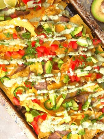 Carne asada nachos with cilantro dip drizzled on top.