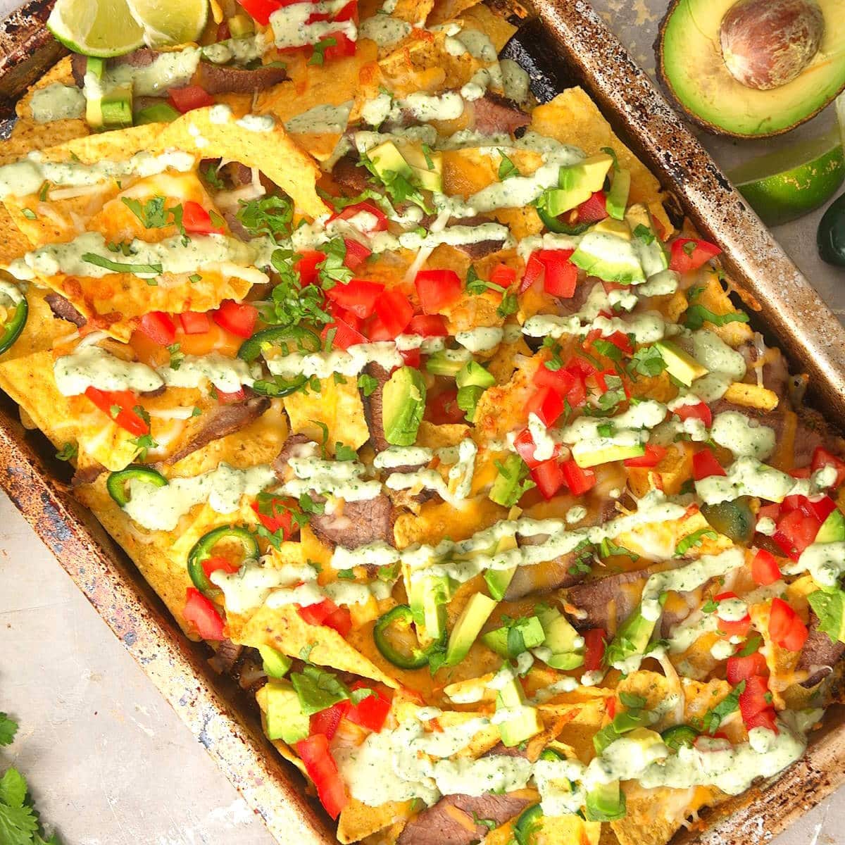Carne asada nachos with cilantro dip drizzled on top.