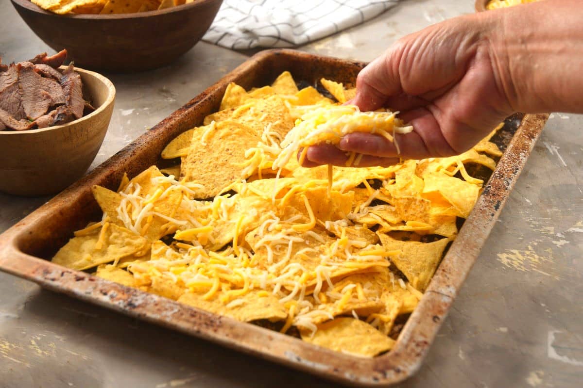 Tortilla chips with shredded cheese on sheet pan.