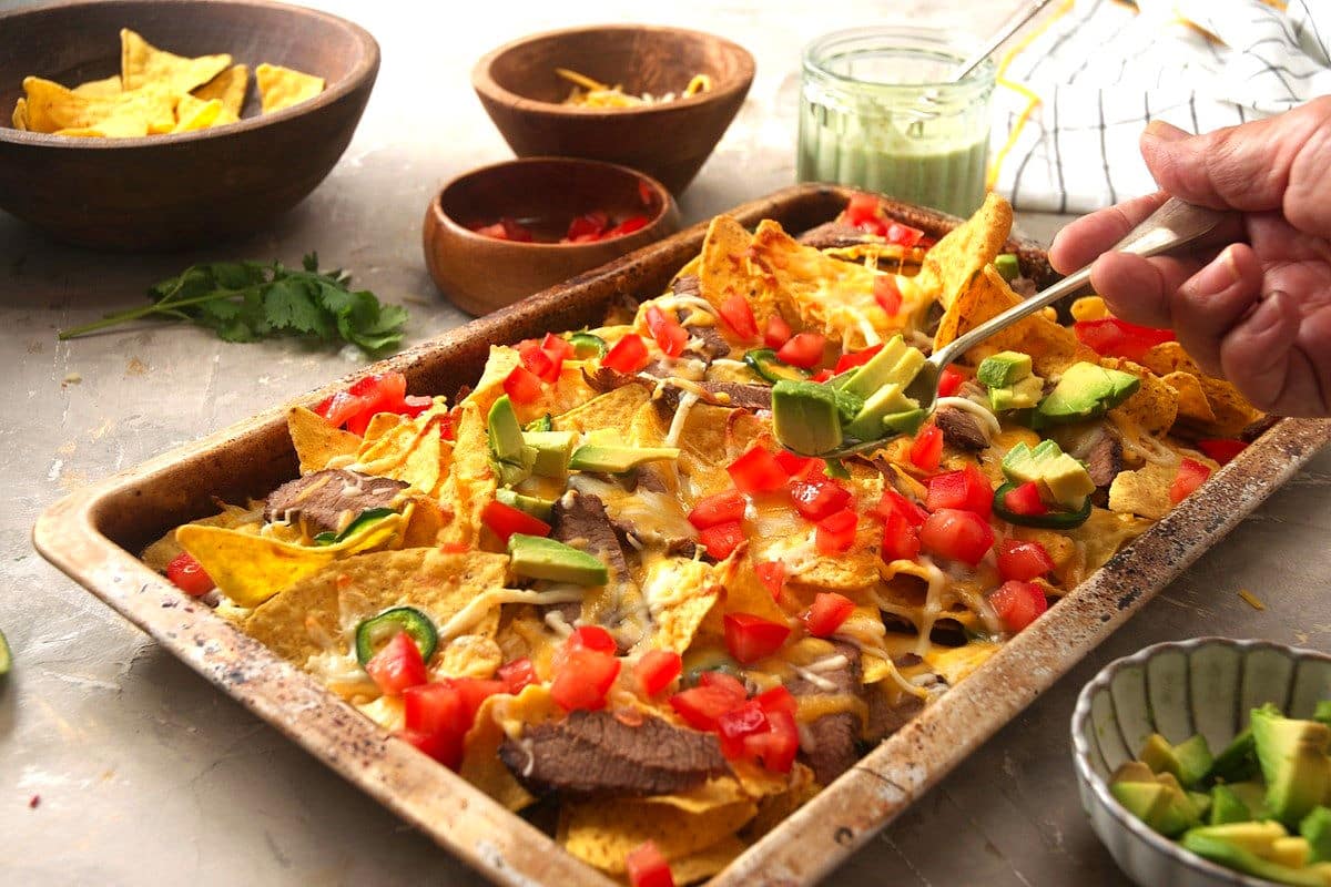 Carne asada nachos in sheet pan with fresh toppings.