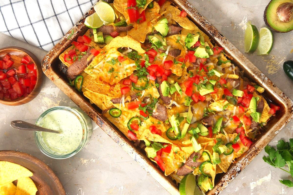 Carne asada nachos in sheet pan with condiments on the side.