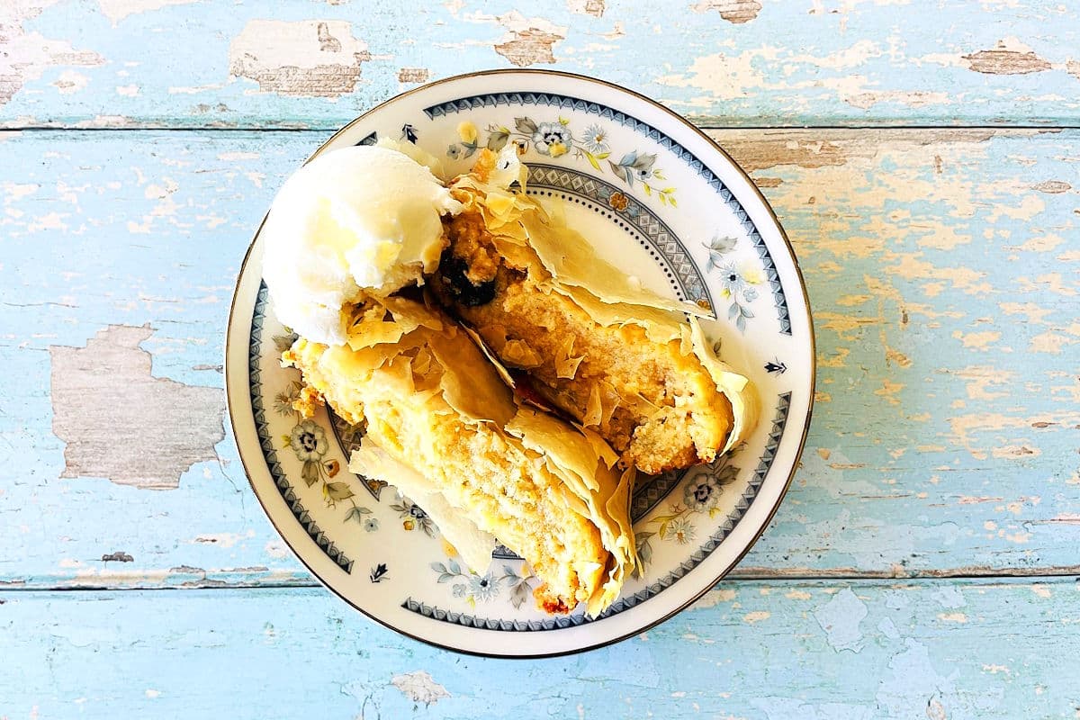 Sliced cheese strudel with a scoop of ice cream on decorative plate.