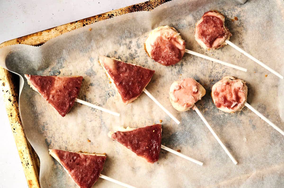 Cheesecake shaped into triangles and balls with treat sticks, chilled on sheet pan.