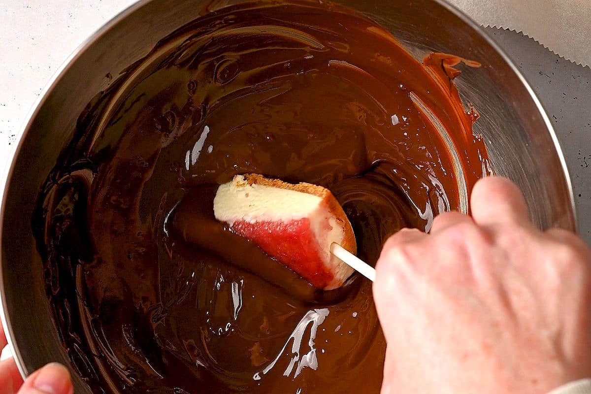 Cheesecake cake pop getting dipped in chocolate.