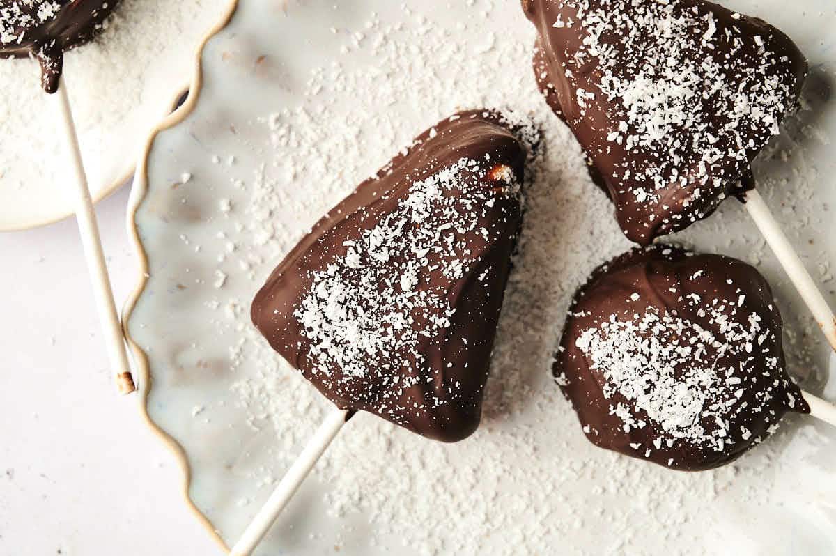 Dark chocolate covered cheesecake cake pops on small white plate.