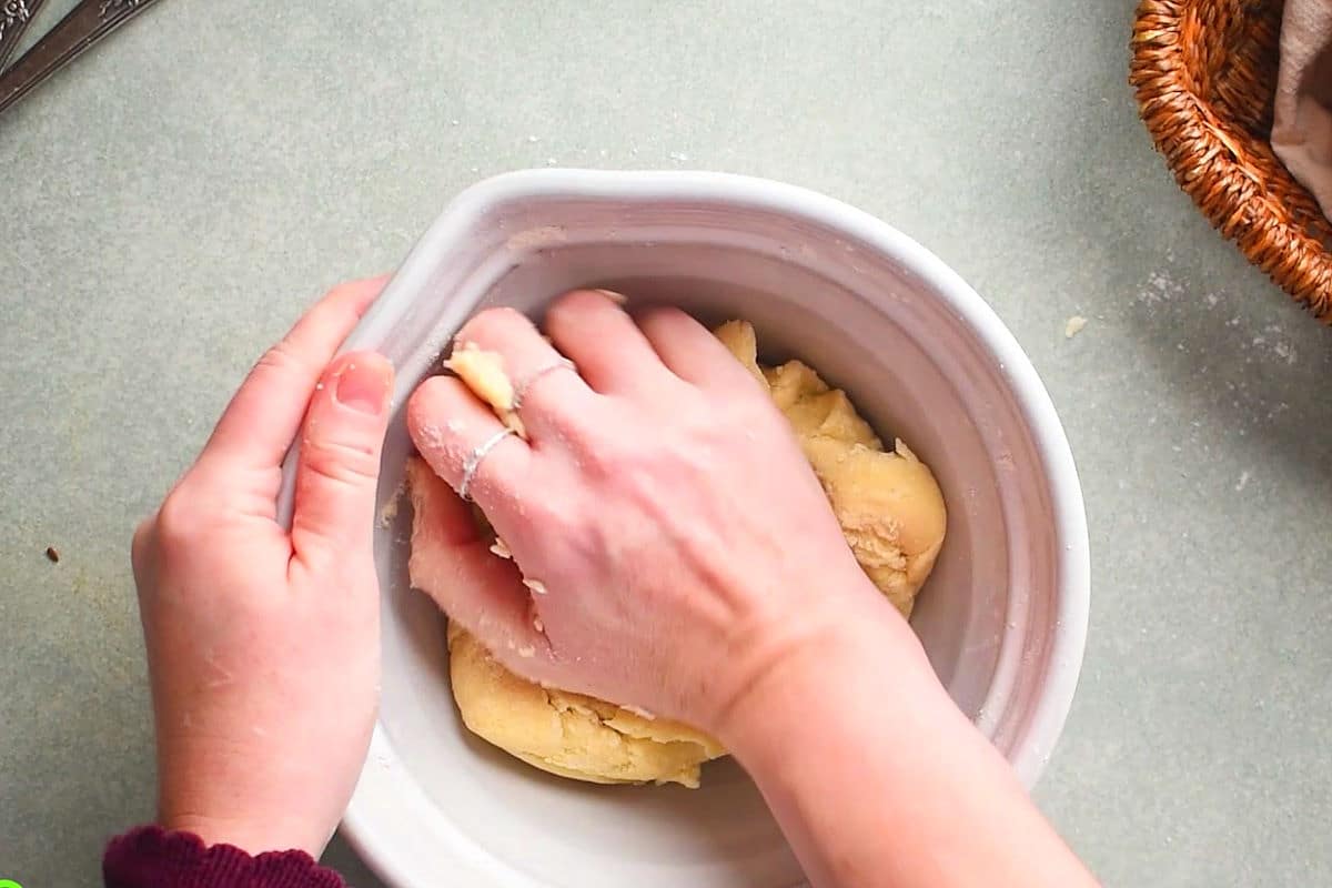 Pastry dough kneaded by woman's hands in bowl.