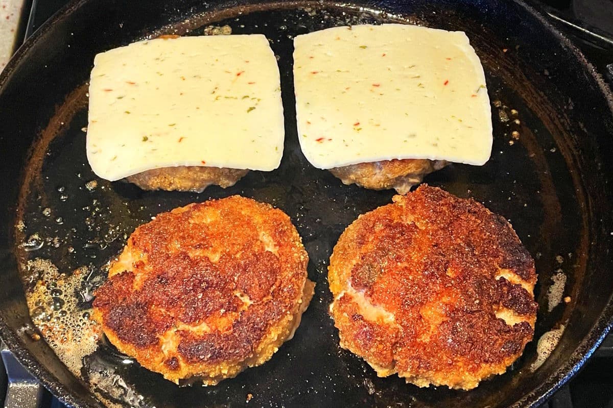 Chicken fried burger patties in pan with cheese slices.