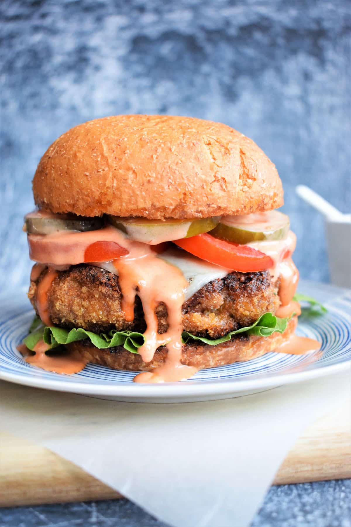 Chicken fried breaded burger on plate with burger sauce dripping down.