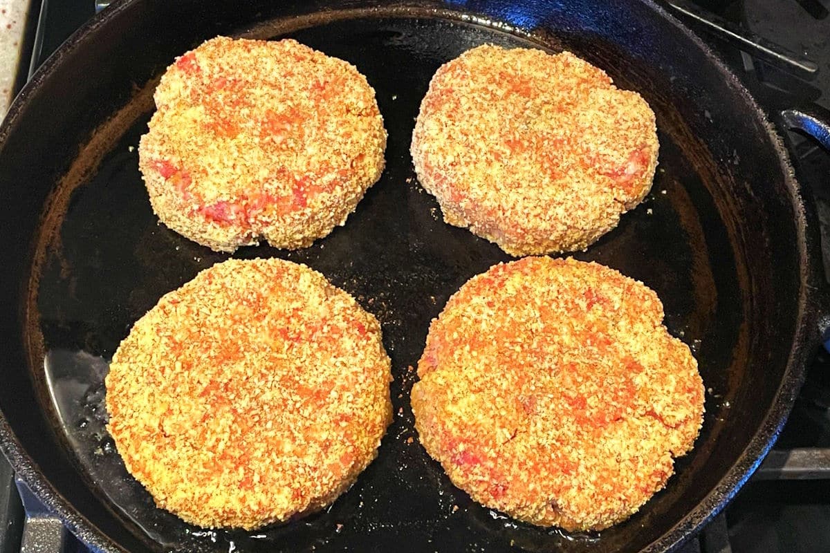 Raw chicken fried burger patties in pan getting fried.