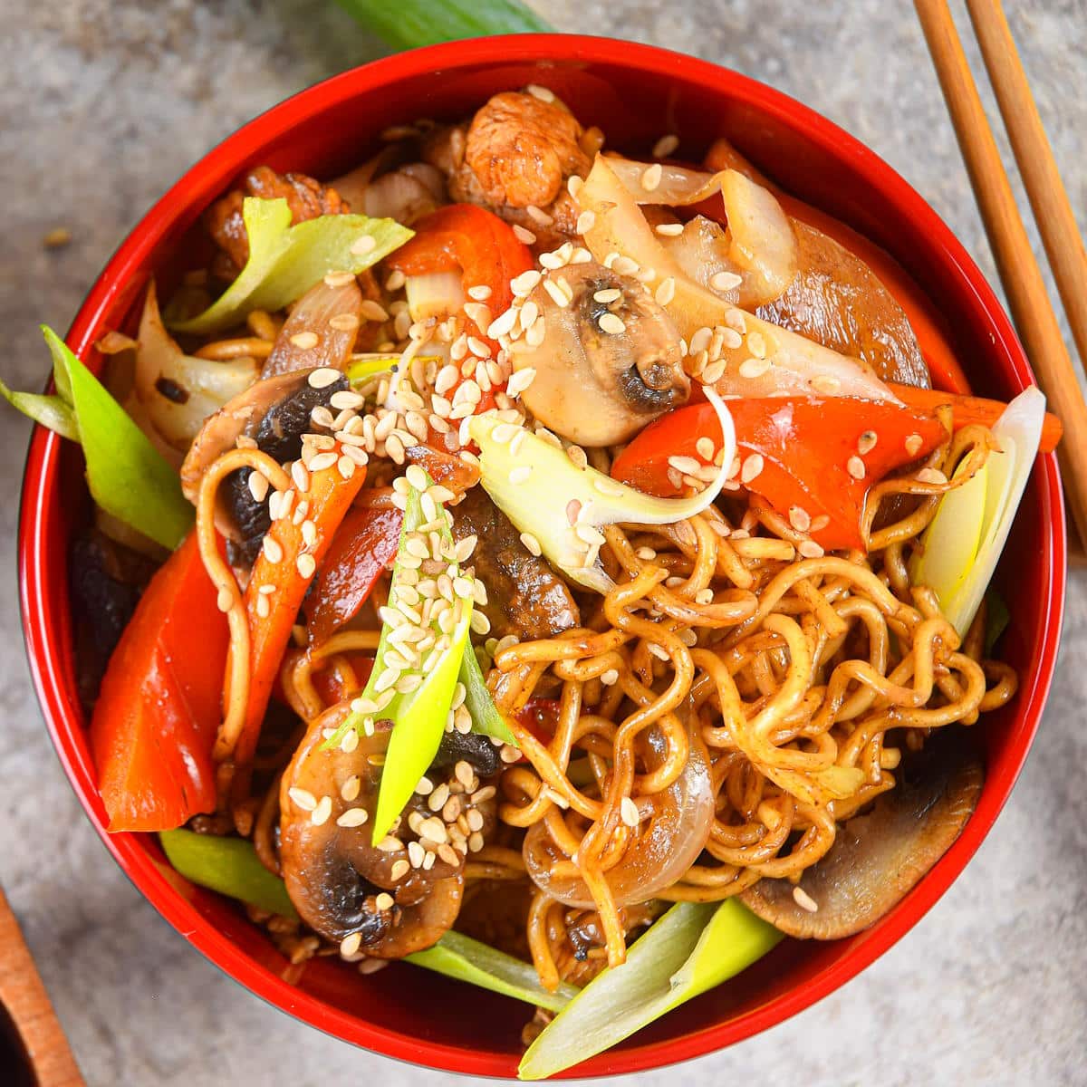 Chicken and vegetable lo mein in red bowl with chopsticks.