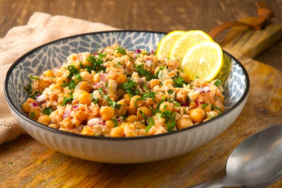 Chickpea and salmon salad in bowl with lemon slices.