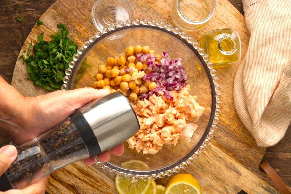 Salmon, onion and chickpeas in bowl and pepper shaker over top.