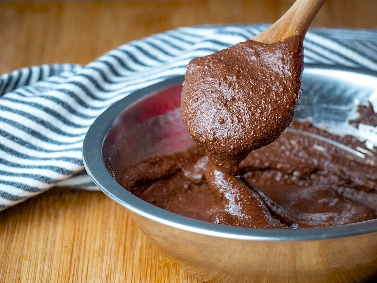 Chocolate truffle mixture in metal bowl with wooden spoon.
