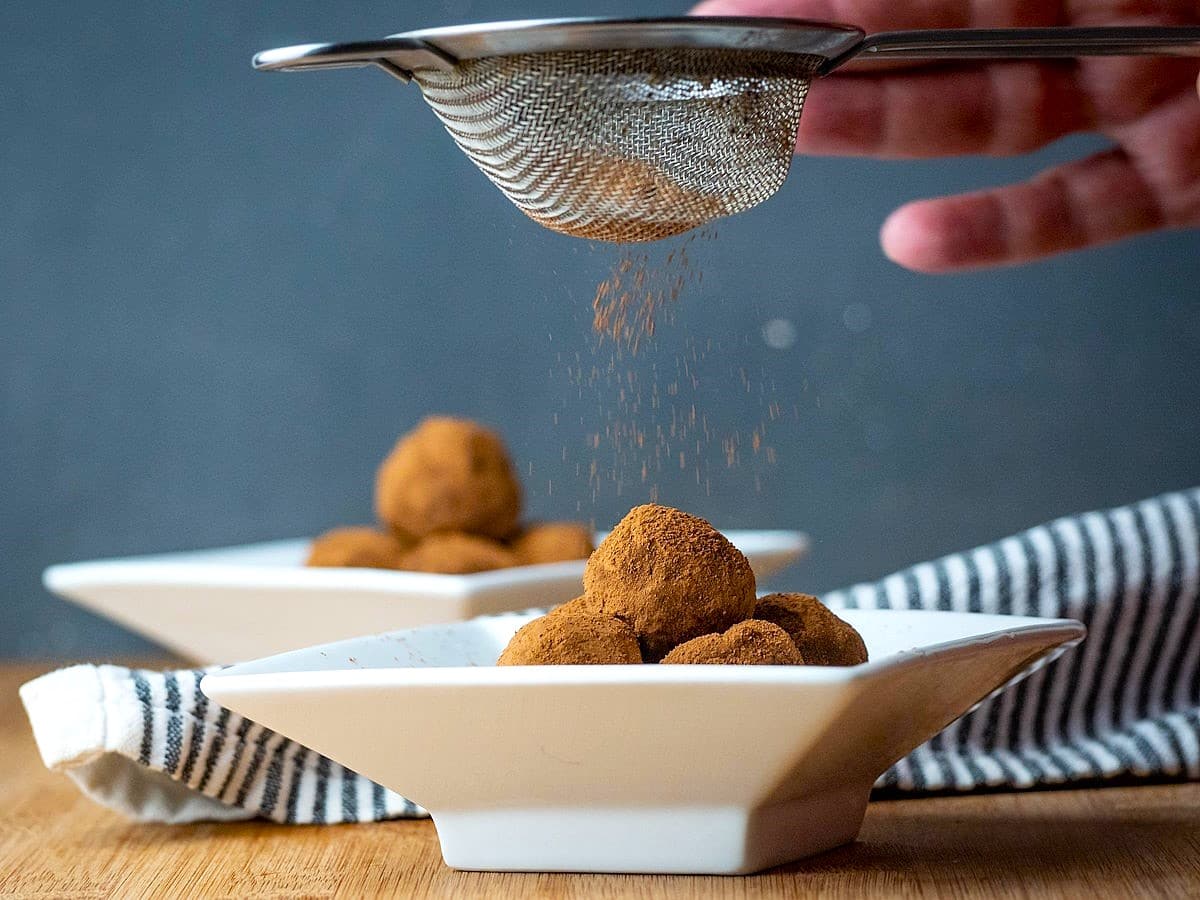 Cocoa powder sprinkled over chocolate truffles with small mesh strainer.