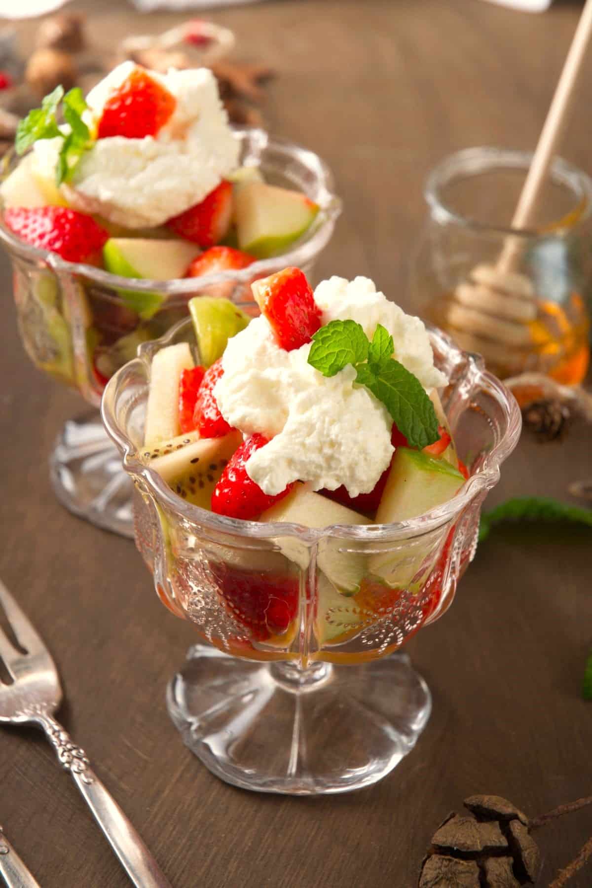 Fruit salad with whipped cream and mint leaves in dessert bowls.