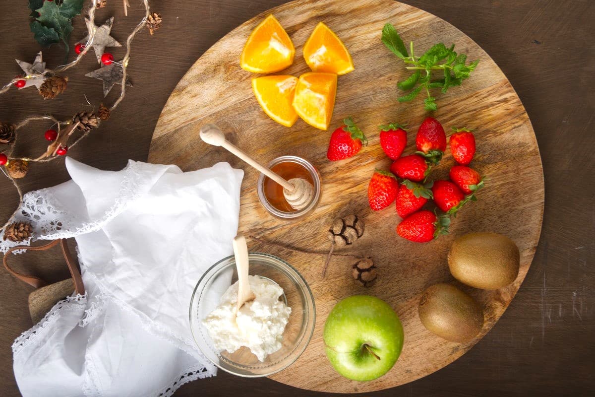 Fruit salad ingredients on wooden board with Christmas decorations.